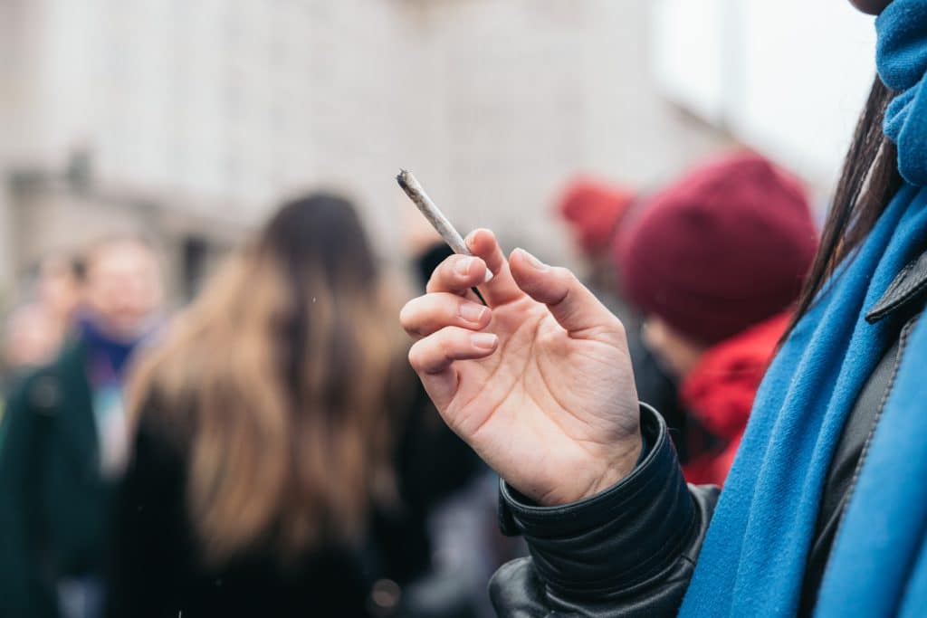 Iemand houdt een joint vast te midden van andere mensen buiten, wat cannabisgebruik in een sociale setting toont.
