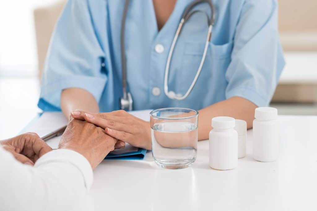 Arts biedt geruststellende ondersteuning aan patiënt tijdens medisch begeleide detox, met water en medicatie op tafel.