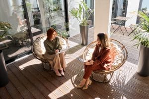 Twee vrouwen in gesprek op een zonnig terras bij een particuliere afkickkliniek in Zuid-Afrika.