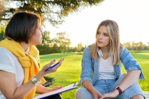 Counselor in gesprek met een cliënt tijdens een individuele therapiesessie in de tuin van een afkickkliniek.